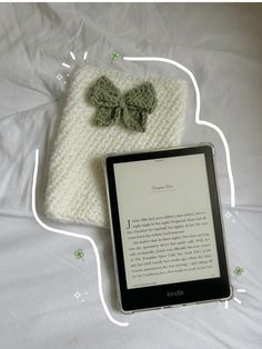 an electronic device with a knitted bow sits on a bed next to a book