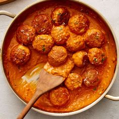 a pan filled with meatballs and sauce on top of a table next to a wooden spoon