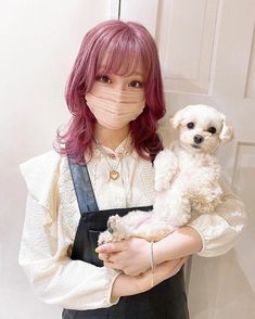 a woman with pink hair holding a white dog in her arms and wearing a face mask