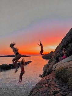 three people jumping off rocks into the water at sunset or dawn with their arms in the air