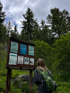 a woman standing in front of a sign on top of a lush green forest filled with trees