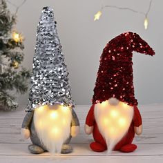 two gnomes are sitting next to each other in front of a christmas tree with lights