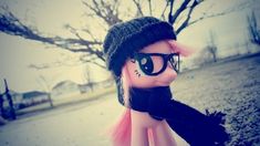 a doll with pink hair and glasses wearing a black hat on the side of a road