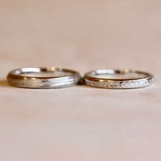 two wedding rings sitting side by side on a table with a light colored surface in the background