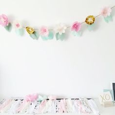 pink and green paper flowers are hanging from a string on a white wall next to a clock