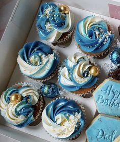 a box filled with blue and white cupcakes on top of a table next to cookies