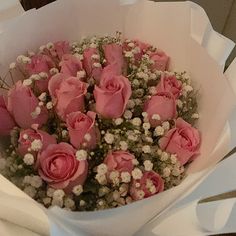 a bouquet of pink roses and baby's breath in a white paper wrapper