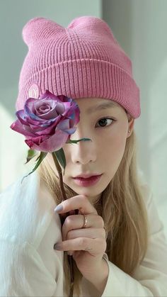 a young woman wearing a pink beanie and holding a flower in front of her face