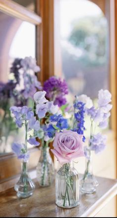 three vases filled with purple and white flowers on a table next to a mirror