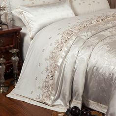 a bed with white and gold comforters on top of it next to a night stand