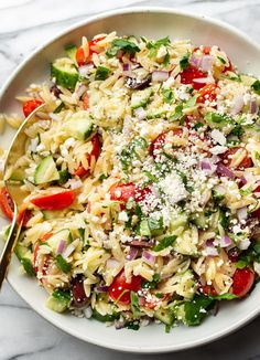 a white bowl filled with pasta salad on top of a marble counter next to a gold spoon