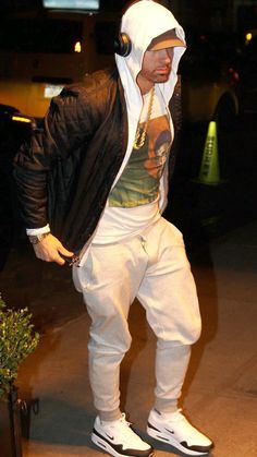 a man in white hoodie and black jacket standing next to a potted plant