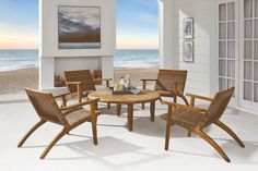 a table and chairs on a porch overlooking the ocean with an open door leading to the beach