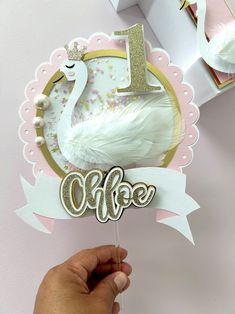 a hand holding a cake topper with a swan and the number one on it