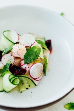 a white plate topped with cucumber, radishes and other veggies