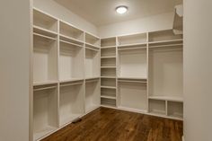 an empty walk - in closet with white shelves and wood flooring on the side