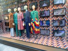 mannequins dressed in colorful clothing on display behind a glass window with multicolored wallpaper