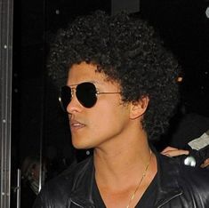 a close up of a person wearing sunglasses and a black leather jacket with an afro