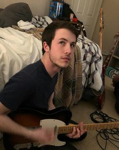 a man sitting on the floor with a guitar in his hand and looking at the camera