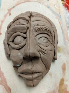 a clay face is sitting on a piece of paper that has been made to look like an old man's head