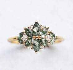 a gold ring with green and white stones in it's center, on a white surface