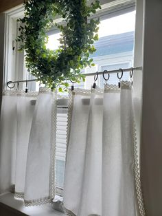 a window with white curtains and a green wreath hanging on the curtain rod in front of it