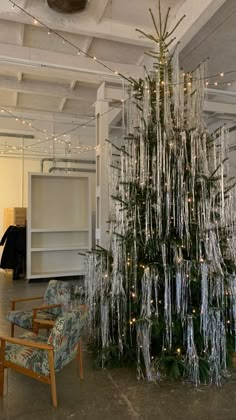 a decorated christmas tree in the middle of a room with chairs and lights hanging from the ceiling