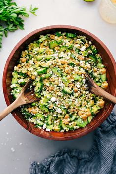 a wooden bowl filled with cucumber and chickpeas salad on top of a table