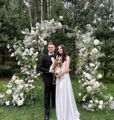 a man and woman standing in front of a flower arch with a dog on it