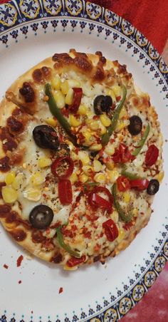 a small pizza on a white plate with blue and yellow border around it, sitting on a red table cloth