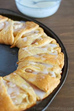 a pastry with icing sitting in a pan next to a glass of milk on a table