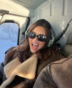 a woman wearing headphones and sunglasses sitting in an airplane with her mouth wide open