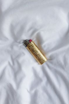 a lighter is laying on top of a white sheet with gold flecks and red trim