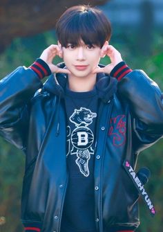 a young man wearing a black leather jacket with his hands on his ears and looking at the camera