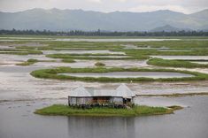 an island in the middle of a lake surrounded by land and water with mountains in the background