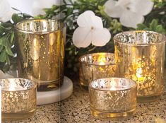 gold colored candles are sitting on a table with flowers in the backgroung