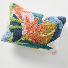 an embroidered pillow with colorful flowers on the front and back, sitting on a white surface