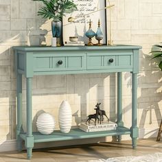 a blue console table with two white vases on it and a framed print above it