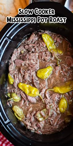 a crock pot filled with meat and peppers on top of a table next to bread