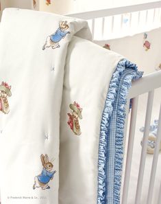 a white crib with a blue ruffle trim and peter rabbit bedding on it