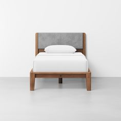 a bed with a gray headboard and white sheets on it, against a white wall