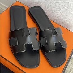 Brand New Hermes Calfskin Oran Sandals In Black 2 Dust Bag, Box Included Color Code : Black Made In Italy These Stylish Slippers Are Crafted Of Polished Smooth Box Calfskin Leather In Black With Insoles Of Leather. The Toe Strap Is A Cross Over Large Hermes H With White Stitching. Black Flat Heel Calf Leather Sandals, Luxury Black Sandals With Leather Sole, Designer Black Leather Sandals, Black Designer Leather Sandals, Luxury Black Flat Heel Sandals, Designer Black Sandals With Leather Sole, Classic Black Flat Heel Sandals, Luxury Black Sandals With Leather Lining, Black Sandals With Leather Lining For Evening