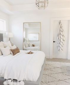 a bedroom with white bedding and pillows in front of a mirror on the wall