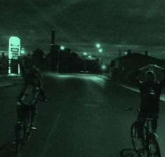 two bicyclists are riding down the street at night with their arms in the air