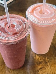 two smoothies with straws are sitting next to each other on a wooden table