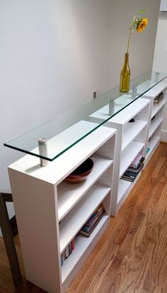 a white shelf with glass shelves and a vase on top