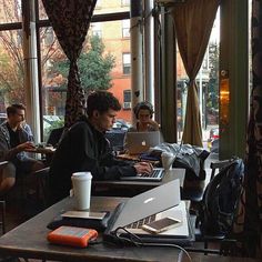 two men sitting at a table with laptops in front of them, one on the phone