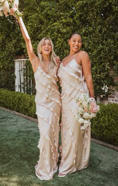 two beautiful women standing next to each other holding bouquets