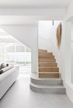 a living room filled with furniture and a staircase leading up to the top floor in front of a white wall