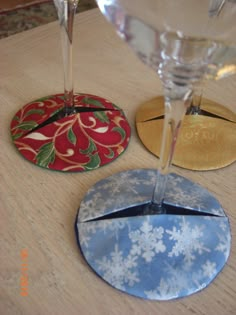 three coasters with different designs on them sitting on a wooden table next to wine glasses